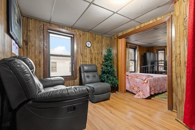 sitting room with a drop ceiling, wooden walls, and wood finished floors