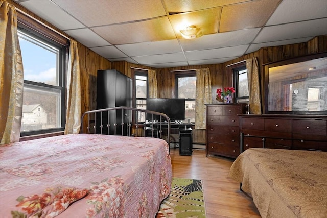 bedroom featuring a drop ceiling, wooden walls, light wood-type flooring, and a baseboard heating unit