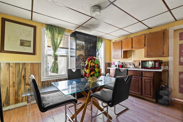dining area with a paneled ceiling, light wood-type flooring, wainscoting, and wooden walls