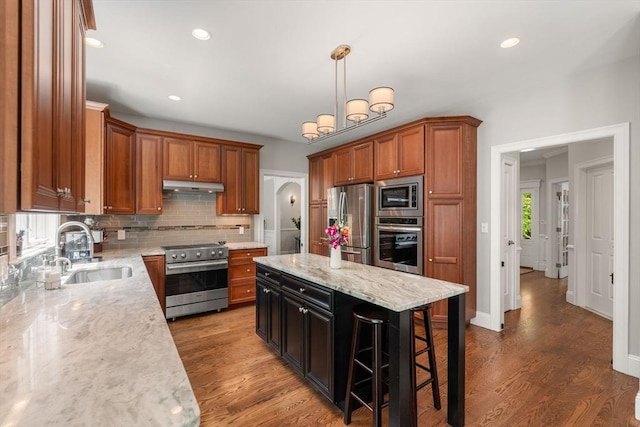 16 Winfield St, Needham, MA 02492 - kitchen with appliances with stainless steel finishes, under cabinet range hood, backsplash, wood finished floors, and a breakfast bar
