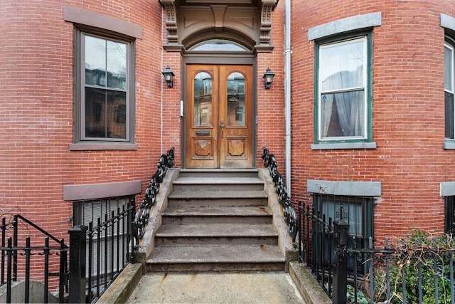 entrance to property featuring fence, french doors, and brick siding