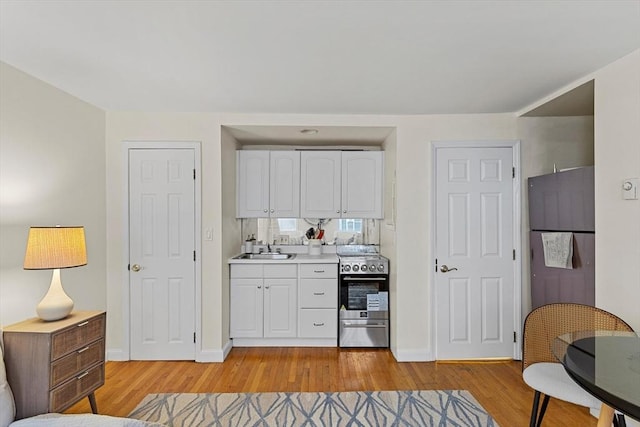 kitchen with light wood-style flooring, a sink, white cabinetry, light countertops, and stainless steel electric stove