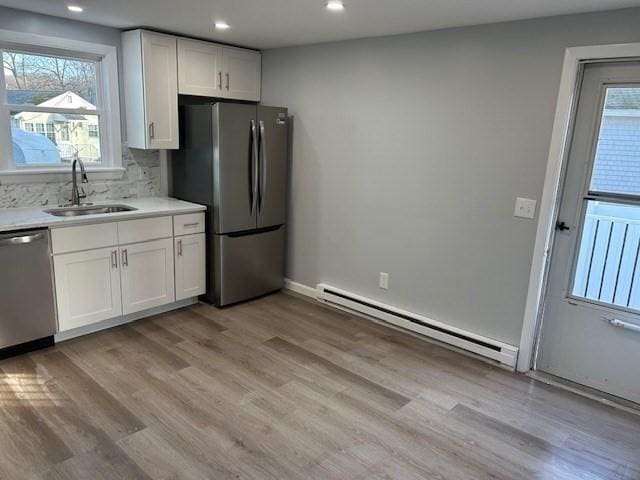 kitchen featuring white cabinetry, sink, a baseboard heating unit, light wood-type flooring, and appliances with stainless steel finishes