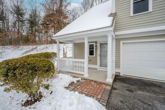 snow covered property entrance with a garage and a porch