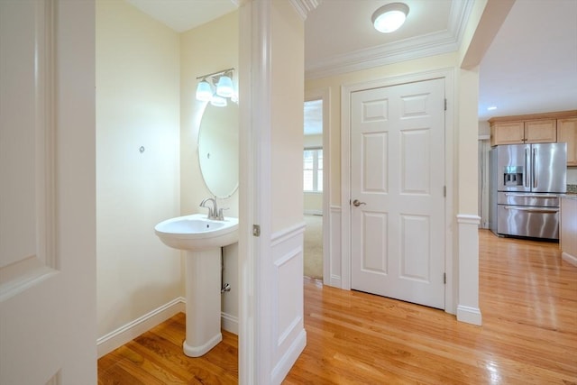 bathroom with a sink, baseboards, wood finished floors, and ornamental molding