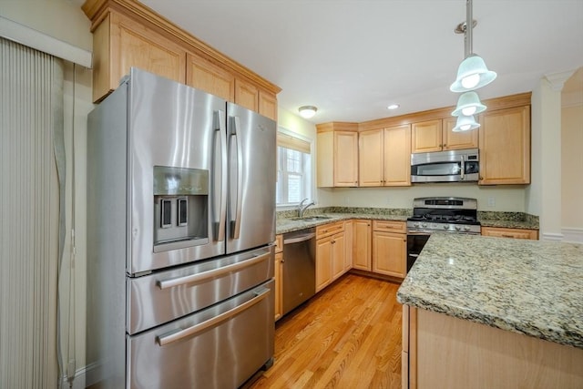 kitchen featuring light brown cabinets, stainless steel appliances, a sink, light wood-style floors, and hanging light fixtures