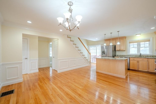 kitchen featuring light stone counters, pendant lighting, stainless steel refrigerator with ice dispenser, light brown cabinets, and a kitchen island