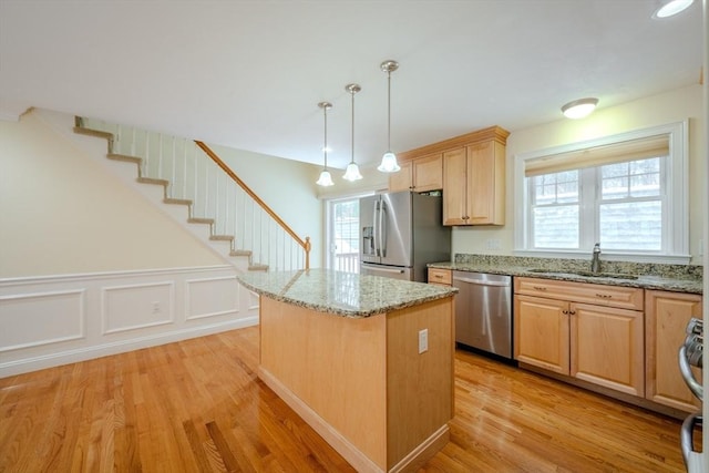 kitchen featuring decorative light fixtures, stainless steel appliances, light wood-style flooring, a sink, and a kitchen island