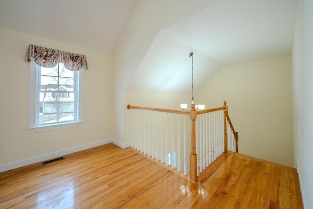 unfurnished room featuring visible vents, vaulted ceiling, wood finished floors, and a chandelier