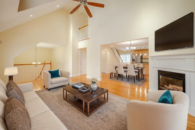 living area with recessed lighting, a glass covered fireplace, high vaulted ceiling, light wood-type flooring, and ceiling fan with notable chandelier