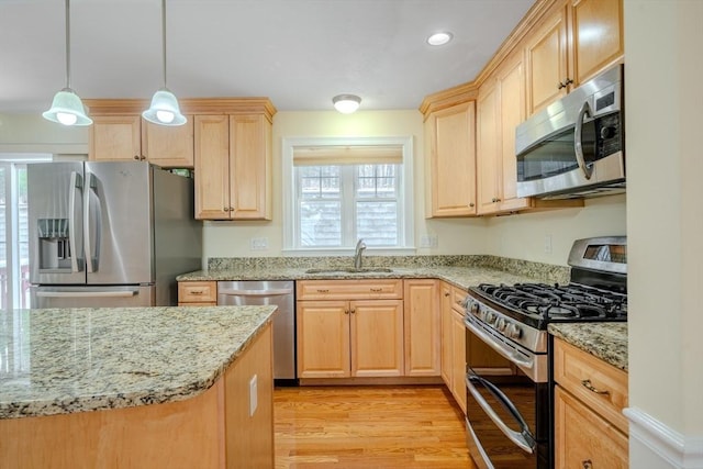 kitchen featuring light wood-style flooring, appliances with stainless steel finishes, light stone counters, hanging light fixtures, and a sink