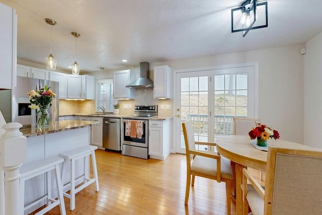 kitchen featuring light wood finished floors, stainless steel appliances, backsplash, a sink, and wall chimney exhaust hood