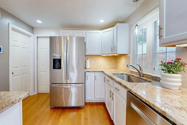 kitchen with light wood finished floors, stainless steel appliances, white cabinetry, pendant lighting, and a sink