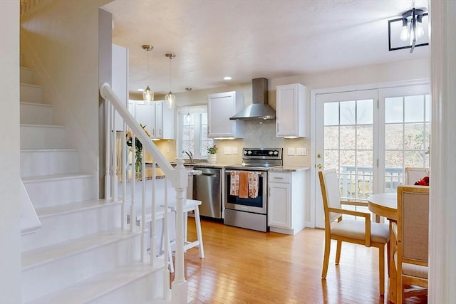 kitchen featuring appliances with stainless steel finishes, light wood-type flooring, wall chimney range hood, and white cabinetry