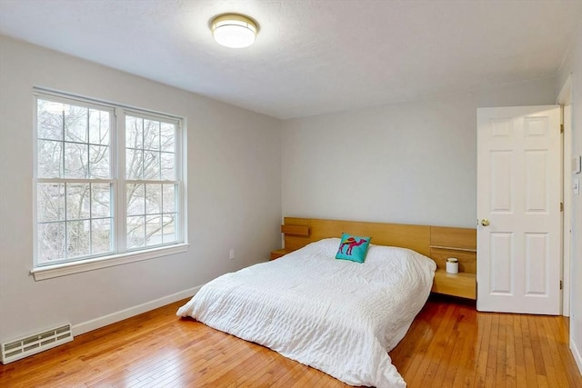 bedroom with hardwood / wood-style floors, visible vents, and baseboards