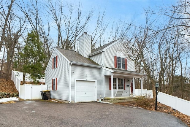 traditional home featuring a shingled roof, a chimney, aphalt driveway, covered porch, and fence