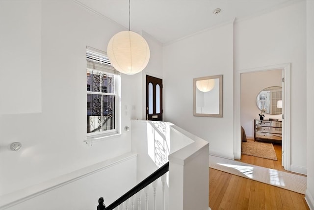 hall featuring an upstairs landing, crown molding, and light wood-type flooring