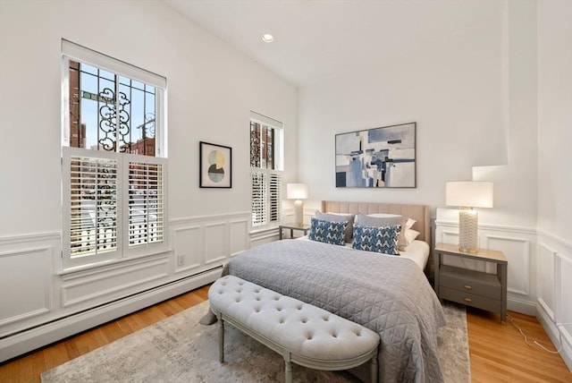 bedroom with a baseboard heating unit, a wainscoted wall, recessed lighting, wood finished floors, and a decorative wall