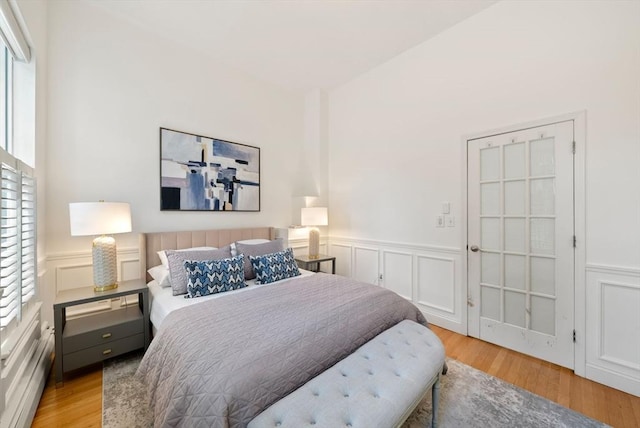 bedroom featuring wood finished floors, wainscoting, and a decorative wall