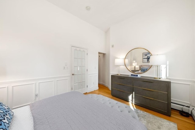 bedroom featuring a wainscoted wall, wood finished floors, and vaulted ceiling