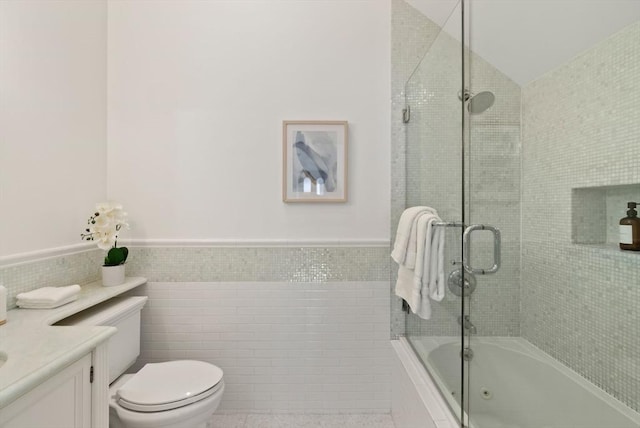 full bathroom featuring tiled shower / bath, a wainscoted wall, toilet, tile walls, and vanity