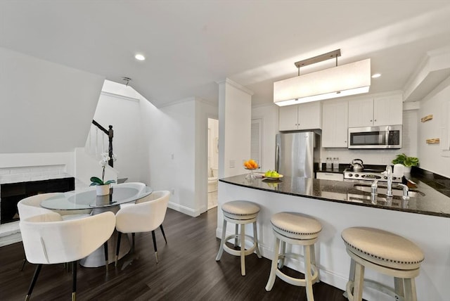 kitchen featuring a breakfast bar, a sink, dark wood finished floors, a peninsula, and appliances with stainless steel finishes