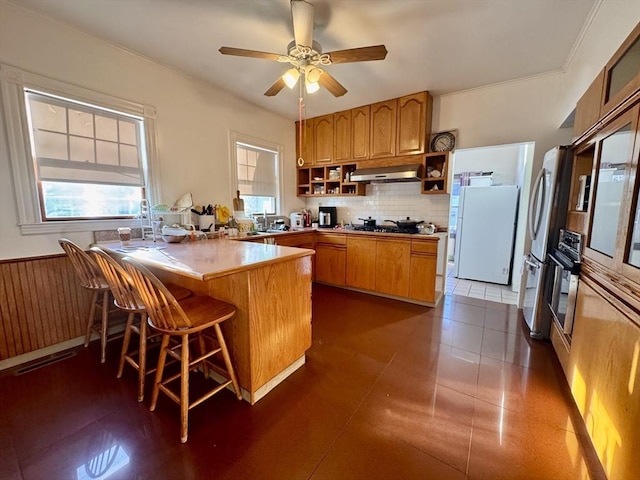 kitchen with ceiling fan, kitchen peninsula, a kitchen bar, dark tile patterned flooring, and appliances with stainless steel finishes