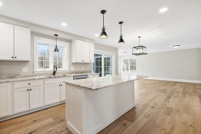 kitchen with white cabinetry, a kitchen island, hanging light fixtures, and light stone counters