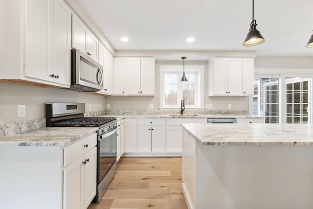 kitchen with appliances with stainless steel finishes, light wood-type flooring, sink, pendant lighting, and white cabinetry