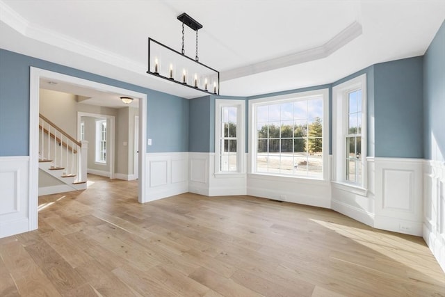 unfurnished dining area with light wood-type flooring, an inviting chandelier, a raised ceiling, and crown molding