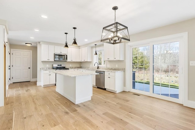 kitchen with white cabinetry, hanging light fixtures, stainless steel appliances, light hardwood / wood-style floors, and a kitchen island