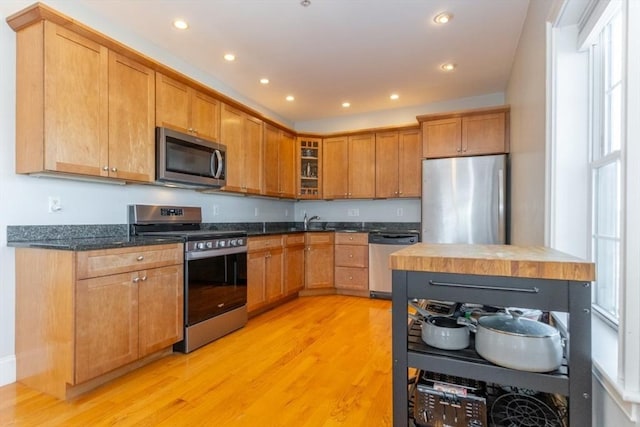 kitchen featuring glass insert cabinets, recessed lighting, light wood-style floors, stainless steel appliances, and a sink