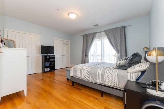 bedroom with light wood-style flooring, visible vents, and two closets