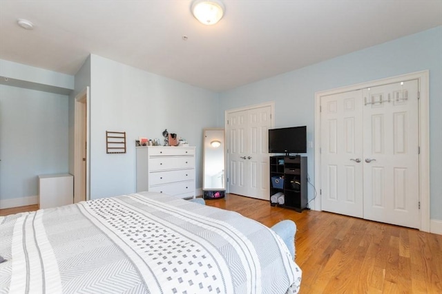 bedroom with baseboards, multiple closets, and light wood finished floors