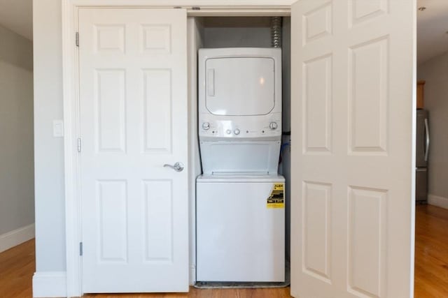 laundry room featuring laundry area, stacked washer and clothes dryer, baseboards, and wood finished floors