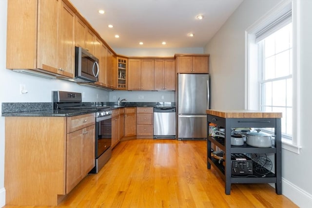 kitchen with baseboards, light wood-style flooring, recessed lighting, glass insert cabinets, and appliances with stainless steel finishes