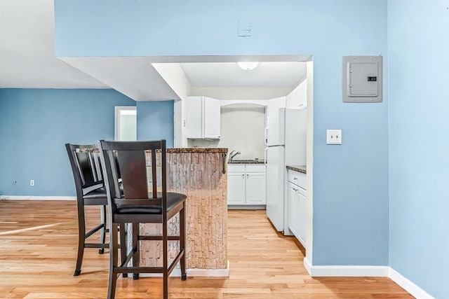 kitchen featuring electric panel, freestanding refrigerator, white cabinets, light wood finished floors, and baseboards