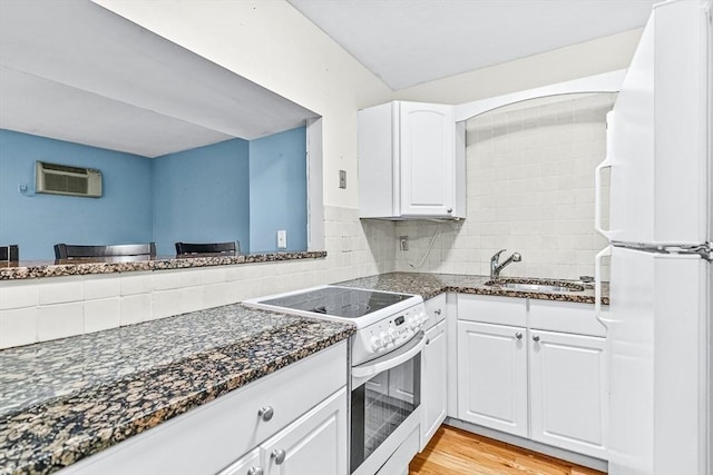 kitchen with white appliances, a wall unit AC, a sink, white cabinetry, and tasteful backsplash