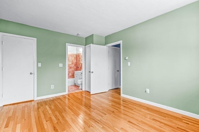 unfurnished bedroom with light wood-style floors, baseboards, and connected bathroom