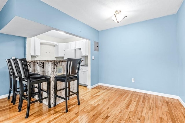 kitchen with baseboards, light wood-style flooring, freestanding refrigerator, decorative backsplash, and white cabinets