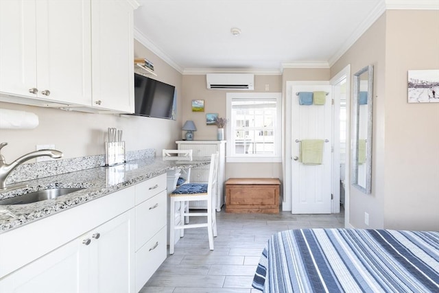 kitchen with light stone countertops, white cabinetry, a sink, and a wall mounted air conditioner