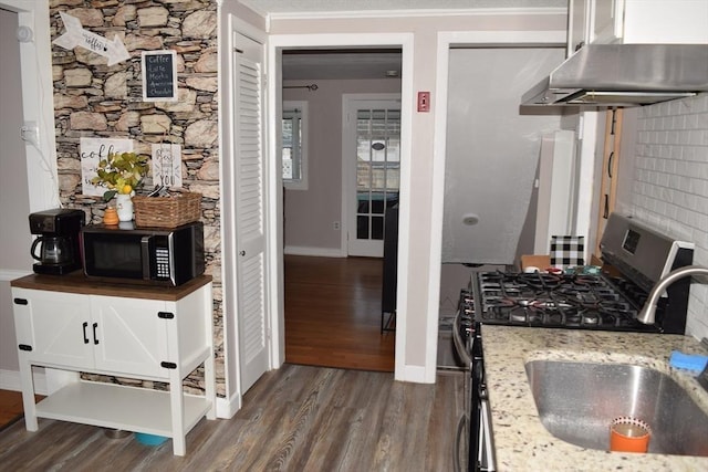 kitchen featuring sink, wall chimney range hood, stainless steel range with gas cooktop, light stone counters, and dark hardwood / wood-style floors