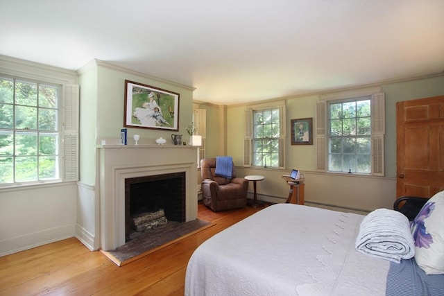 bedroom with light wood-type flooring, crown molding, and a baseboard heating unit