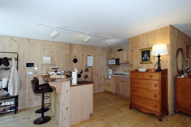 kitchen featuring a breakfast bar, wood walls, light wood-type flooring, and light brown cabinetry