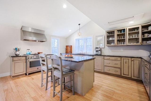 kitchen featuring light wood-type flooring, high end range, wall chimney exhaust hood, and a kitchen bar