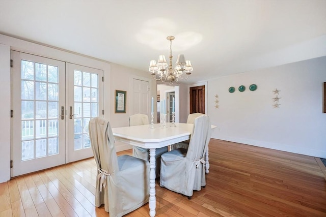 dining area featuring light wood-style flooring, french doors, a notable chandelier, and baseboards
