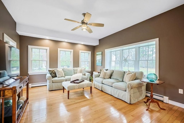 living room with baseboards, baseboard heating, light wood-type flooring, and a ceiling fan