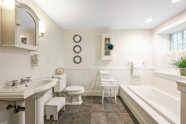 full bathroom featuring tile patterned floors, toilet, a garden tub, and a wainscoted wall