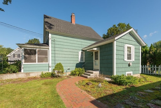 rear view of house with a yard, a chimney, fence, and roof with shingles