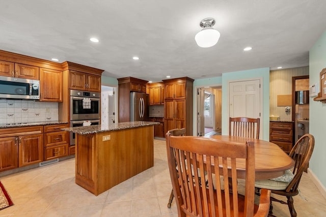 12 Checkerberry Cir, Sudbury, MA 01776 - kitchen with appliances with stainless steel finishes, a center island, brown cabinets, decorative backsplash, and dark stone countertops